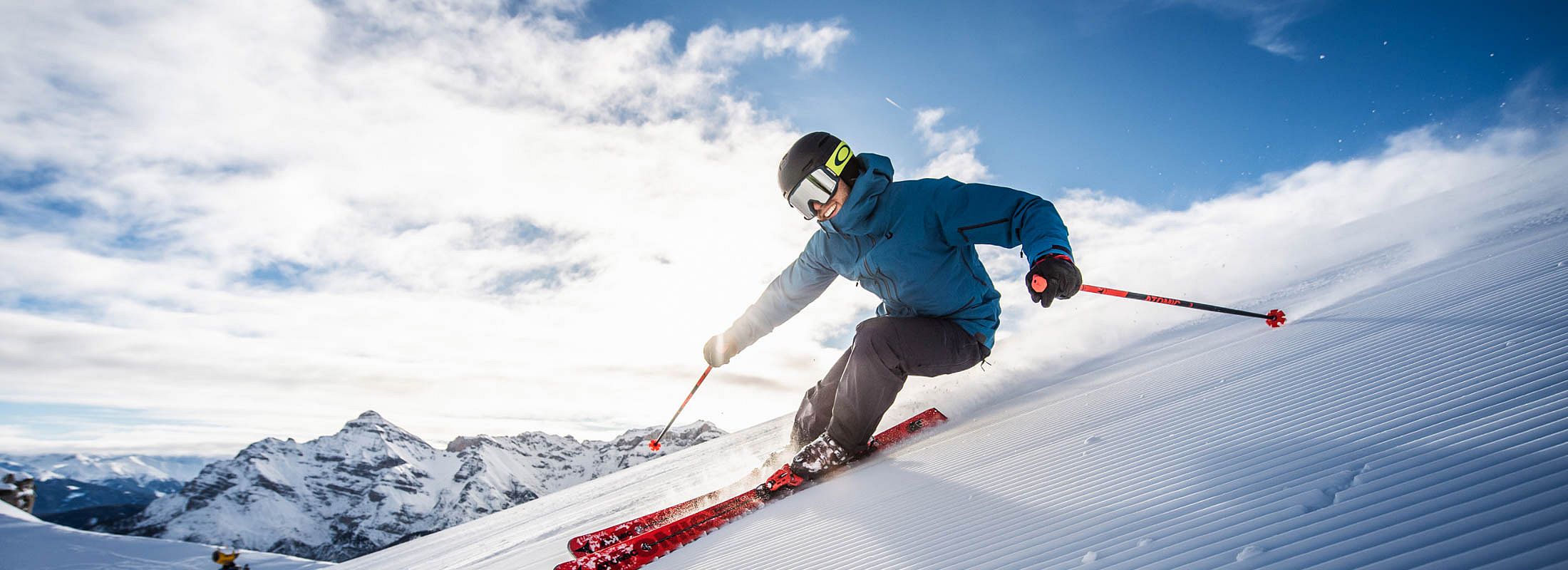 Sportlicher Skifahrer fährt rasant eine präparierte Piste in verschneiter Alpenkulisse hinunter