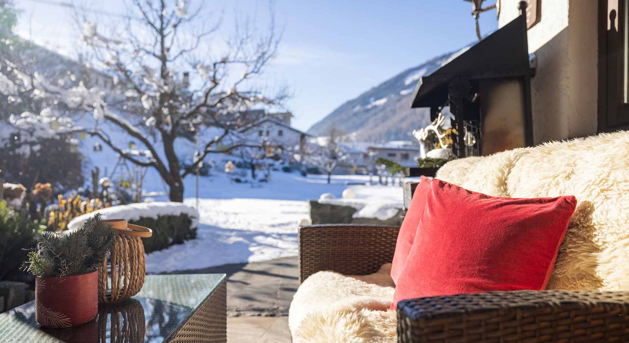 Kuschelige Winterterrasse mit Fell, roten Kissen und Blick auf die verschneite Winterlandschaft