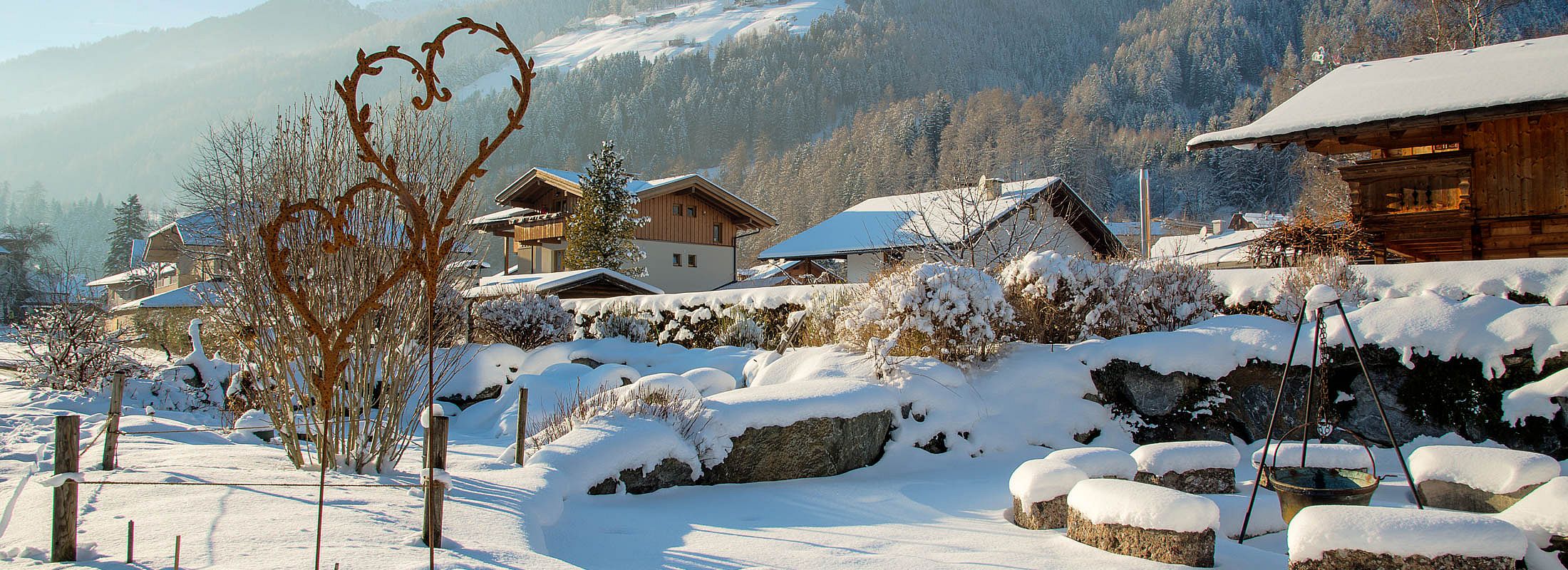 Romantischer verschneiter Garten mit Herzskulptur, Feuerstelle und Bergblick im Winterlicht