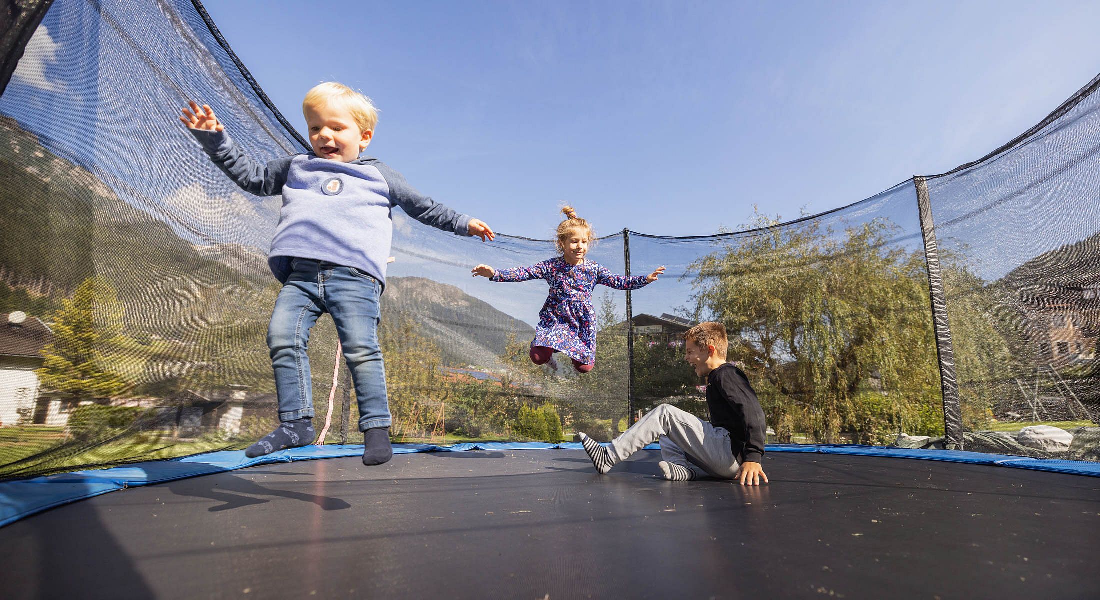 Kinder toben auf einem großen Trampolin mit Bergkulisse im Hintergrund