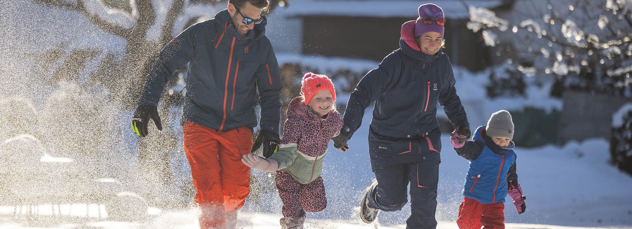 Familie läuft lachend durch den Schnee und genießt gemeinsame Zeit im Winterurlaub