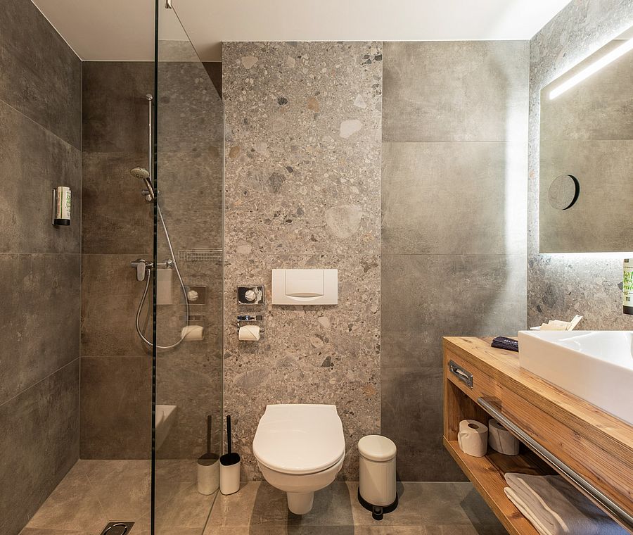 Modernes Badezimmer im Hotel Auenhof mit Regendusche, WC, Natursteinfliesen und beleuchtetem Spiegel.