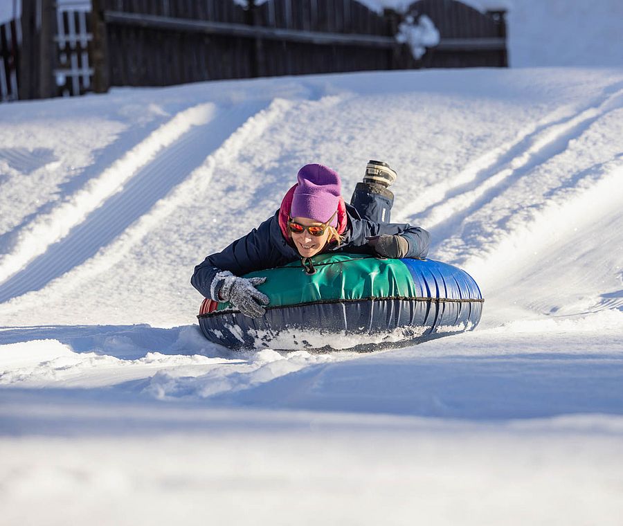 Erwachsene Person rutscht lachend mit einem Reifen den Schneehang hinunter