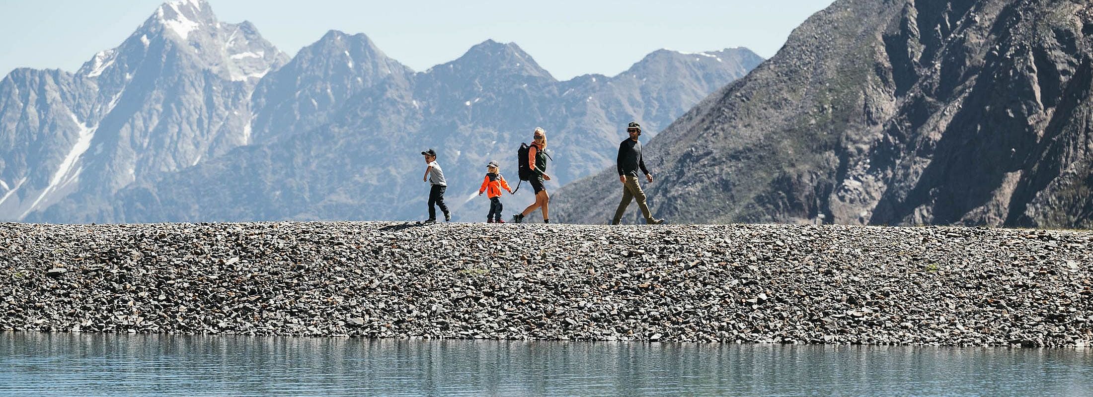 Family hiking on a gravel dam with impressive snow-covered mountain peaks in the background